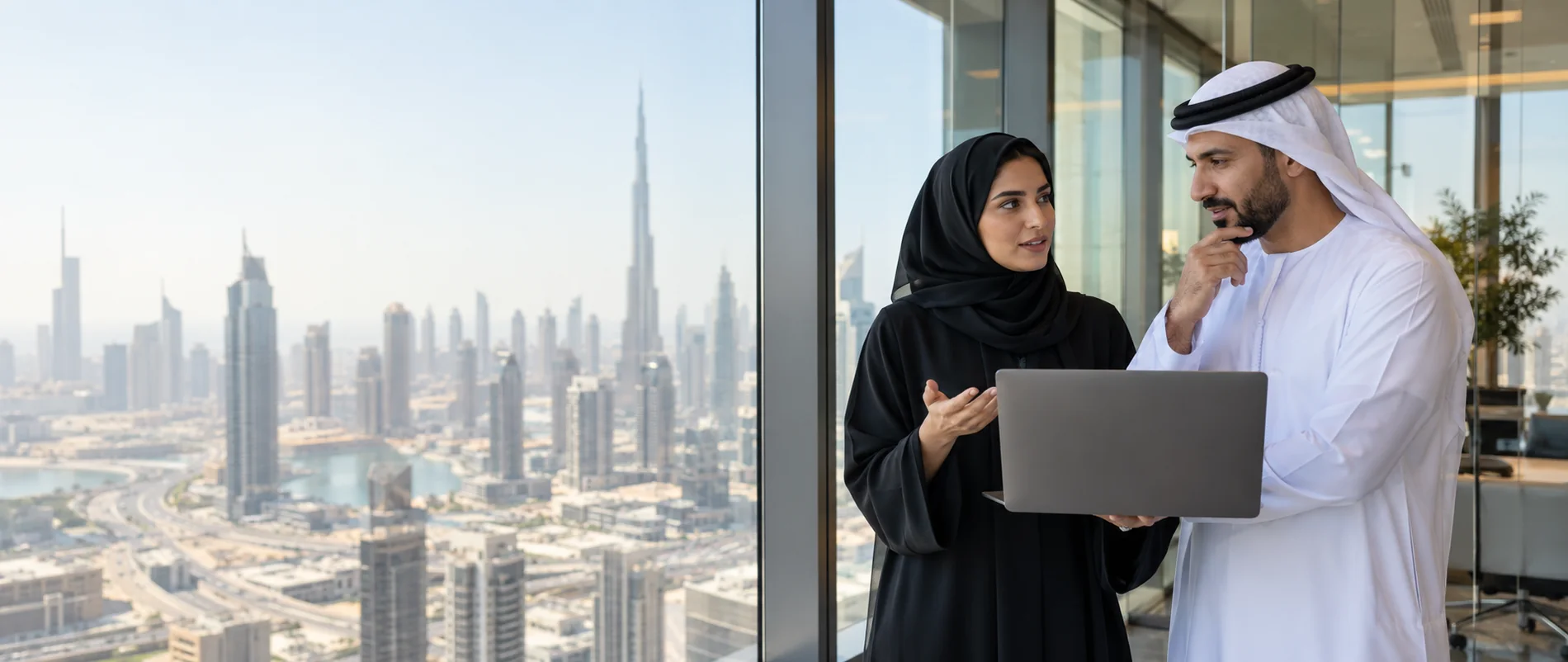 Two colleagues talking by an office window overlooking the Dubai skyline
